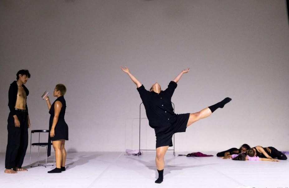 Dancer balancing on one leg, arms raised, white stage